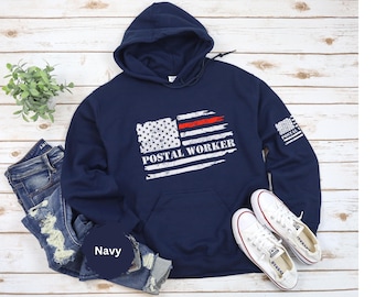 Puede incluir: Sudadera con capucha azul marino de "Postal Worker" con un diseño de bandera estadounidense desgastada y el texto "POSTAL WORKER" en blanco. Cuenta con una franja roja y un pequeño gráfico de bandera en la manga. Incluye bolsillo delantero y capucha con cordón.