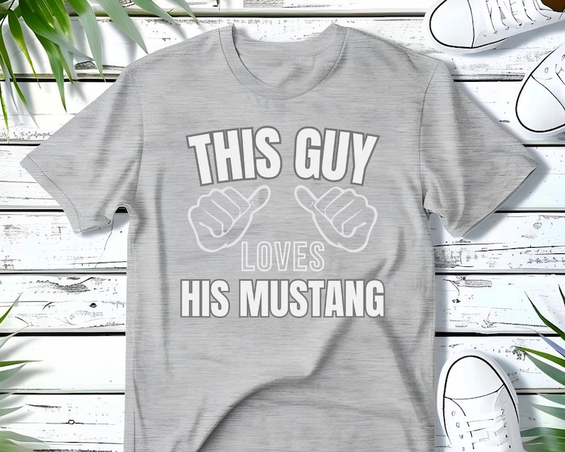 May include: Gray t-shirt with the text "This Guy Loves His Mustang" in white. The text is surrounded by two thumbs up symbols.