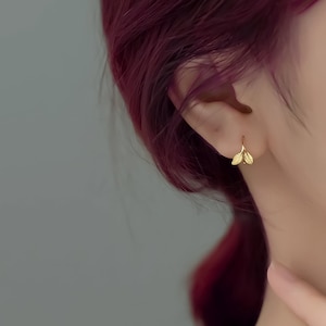 以下が含まれることがあります： 繊細なデザインのゴールドリーフイヤリング。イヤリングは小さくシンプルで、毎日のアクセサリーに最適です。