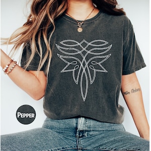 May include: A dark gray t-shirt with a white embroidered design on the front. The design is a stylized geometric pattern with a pointed bottom.
