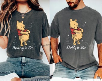 Puede incluir: Dos camisetas grises con un diseño de dibujos animados de Winnie de Pooh. Las camisetas tienen el texto "Mommy to Bee" y "Daddy to Bee" impreso en ellas.