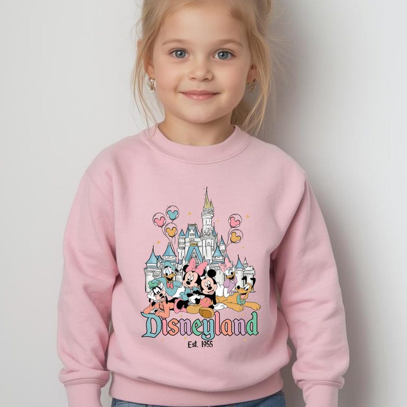 Puede incluir: Sudadera rosa claro con un gr&aacute;fico de Disneyland. El gr&aacute;fico incluye un castillo, Mickey y Minnie Mouse, el Pato Donald y Goofy. Tambi&eacute;n se ve el texto "Disneyland Est. 1955".