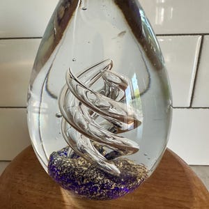 May include: A clear glass paperweight with a silver swirl inside. The bottom of the paperweight is filled with blue and gold glitter.