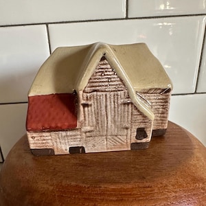 Könnte beinhalten: Eine Keramik-Scheunenfigur mit brauner und beigefarbener Außenseite, einem roten Dach und einer braunen Tür. Die Scheune hat eine strukturierte Oberfläche und ist ein dekoratives Stück.