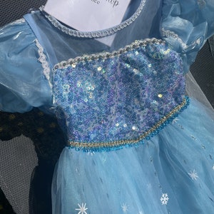 Close-up of an Elsa dress's bodice, showcasing its sequined detail and blue-purple gradient beneath a string of pearls.