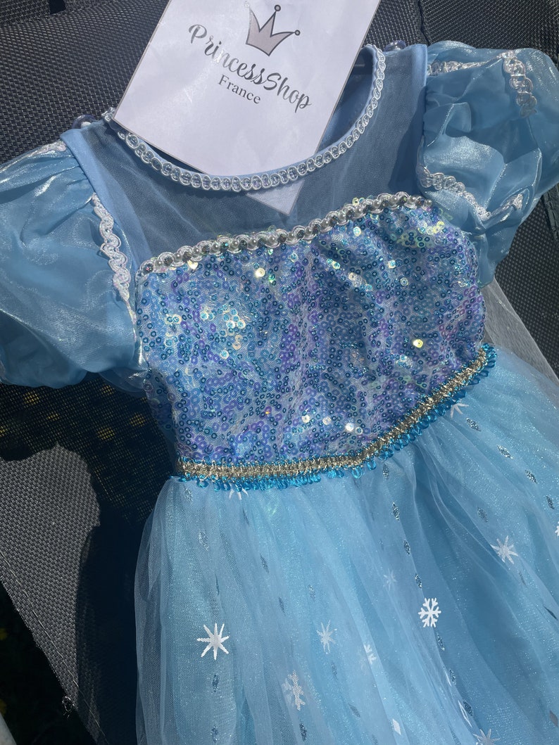 Close-up of an Elsa dress's bodice, showcasing its sequined detail and blue-purple gradient beneath a string of pearls.