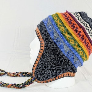 May include: A knitted hat with ear flaps and braided tassels. The hat has a dark blue base and a striped pattern of blue, green, yellow, orange, and purple. The ear flaps and tassels are multi-coloured.