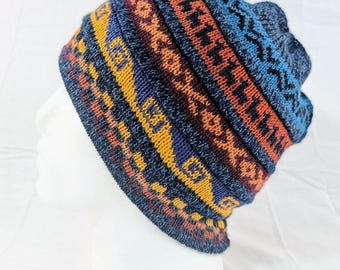 Può includere: Un berretto lavorato a maglia con un motivo geometrico colorato. Il cappello presenta fasce blu, arancioni, gialle e bordeaux. Il cappello è esposto su una testa di manichino bianca.