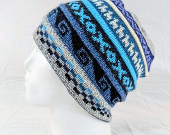 Può includere: Un berretto lavorato a maglia nei toni del blu, grigio e bianco. Il cappello presenta un motivo geometrico con strisce e losanghe. Il cappello è esposto su una testa di manichino bianca.