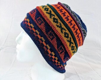 Può includere: Un berretto lavorato a maglia colorato con un motivo geometrico. Il cappello presenta una base blu scuro con fasce arancioni, gialle, verdi e viola. Il design include motivi e forme ripetute, creando un aspetto vibrante e strutturato.