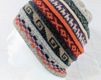 Può includere: Un berretto lavorato a maglia colorato con un motivo geometrico. Il cappello presenta fasce arancioni, viola, verdi e grigie, con un motivo al centro. Il berretto è esposto su una testa di manichino bianca.