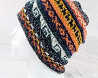 Può includere: Un berretto lavorato a maglia colorato con un motivo geometrico. Il cappello presenta un mix di colori blu scuro, arancione, bianco e giallo. Il cappello è esposto su una testa di manichino bianca.