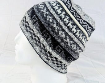 Può includere: Un berretto lavorato a maglia nei toni del grigio, nero e bianco, con un motivo geometrico. Il cappello ha un bordo ripiegato e una striscia bianca. Il cappello è esposto su una testa di manichino bianca.