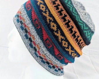 Può includere: Un berretto lavorato a maglia colorato con un motivo geometrico. Il cappello presenta fasce grigie, rosse, verde acqua, arancioni e verdi. Il cappello è esposto su una testa di manichino bianca.