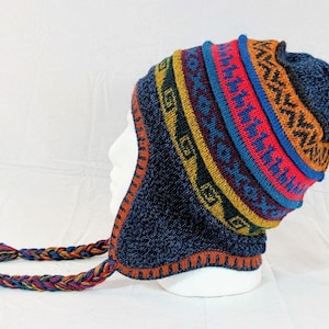 May include: A blue knitted hat with ear flaps and braided tassels. The hat has a colourful geometric pattern in red, yellow, and blue. The hat is displayed on a white mannequin head.