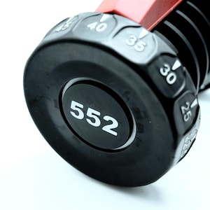 May include: Close-up of a black and red tool with a rotating dial. The dial has white numbers indicating measurements, with the number "552" prominently displayed. The tool's design includes a textured grip and a metallic red component.