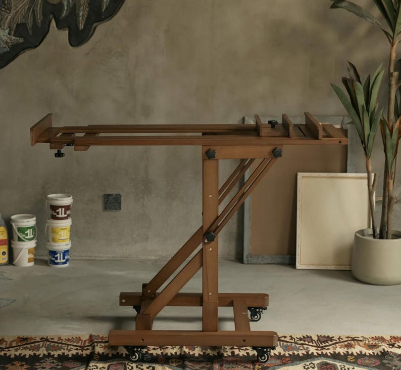 May include: A wooden easel with adjustable height and angle, featuring a brown finish and black hardware. The easel is on wheels and has a canvas holder.