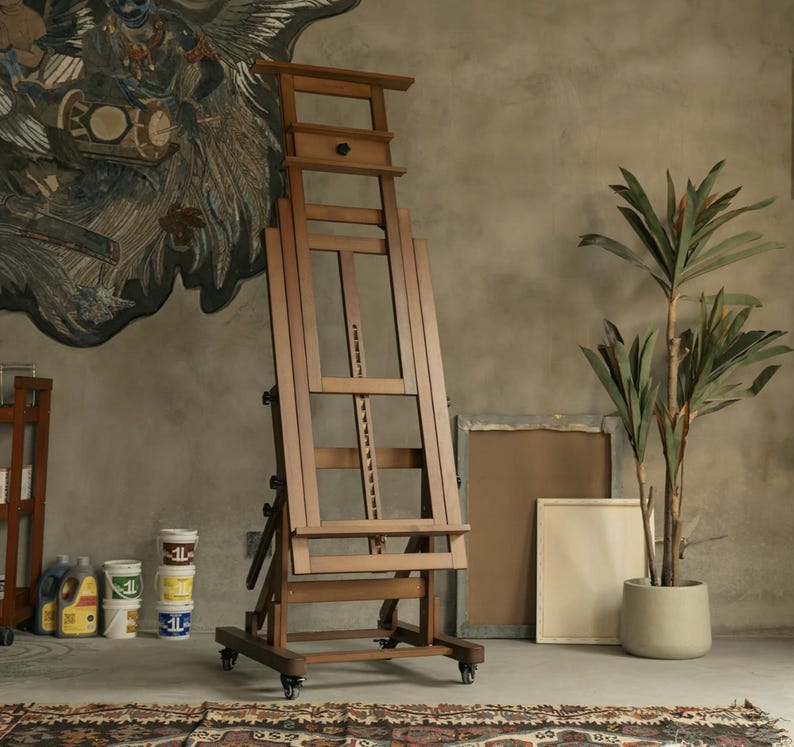 May include: A wooden artist's easel with adjustable height and a canvas holder. The easel has wheels for easy movement and is made of dark brown wood.