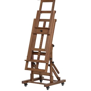 May include: A brown wooden artist's easel with a chain and pulley system for adjusting the height. It features a drawer and a shelf for supplies. The easel is on wheels and can be moved around easily.
