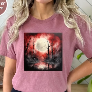 May include: Heather Mauve t-shirt with a square graphic of a spooky forest scene. The artwork shows a full moon, bare trees, and a red and black colour palette. The shirt is a dusty rose colour.