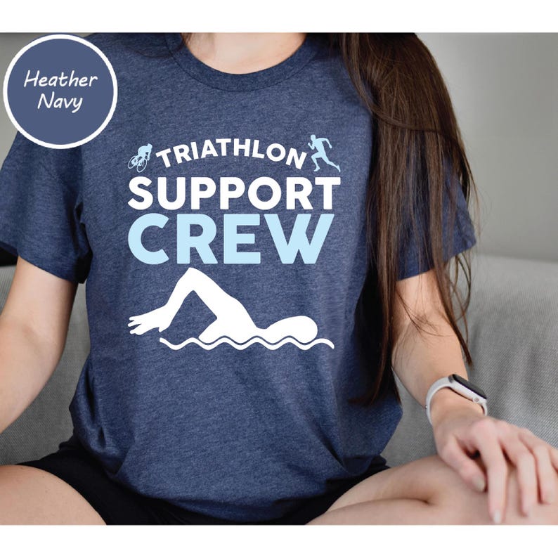 May include: Heather navy blue t-shirt with the words "TRIATHLON SUPPORT CREW" in white and light blue. The shirt features a swimmer, a cyclist, and a runner graphic. The shirt is made of a soft material.