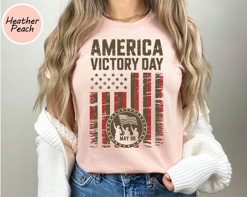 May include: A light pink t-shirt with the text "AMERICA VICTORY DAY" in dark brown. The design includes a distressed American flag graphic and a circular emblem with figures holding a flag, with "MAY 08" below.