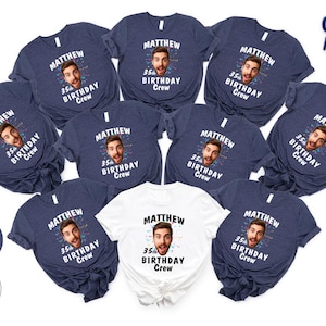 May include: A collection of navy blue and white t-shirts. Each shirt features a face graphic with the name "Matthew" and the text "35th Birthday Crew". The shirts are arranged on a white surface.
