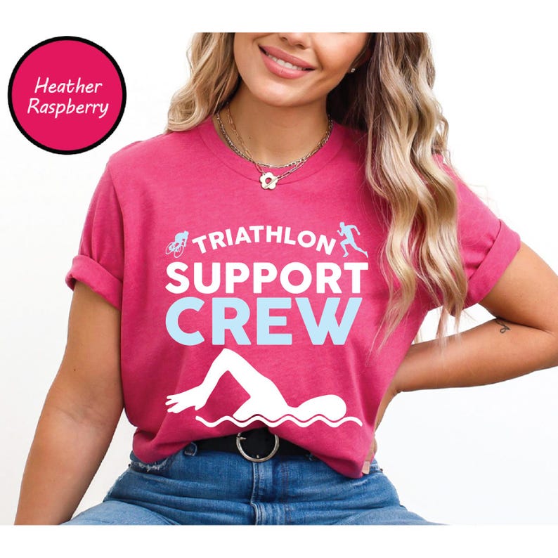 May include: Heather raspberry t-shirt with the text "TRIATHLON SUPPORT CREW" in white and light blue. The design includes a bicycle, a runner, and a swimmer. The shirt is a crew neck and has rolled-up sleeves.