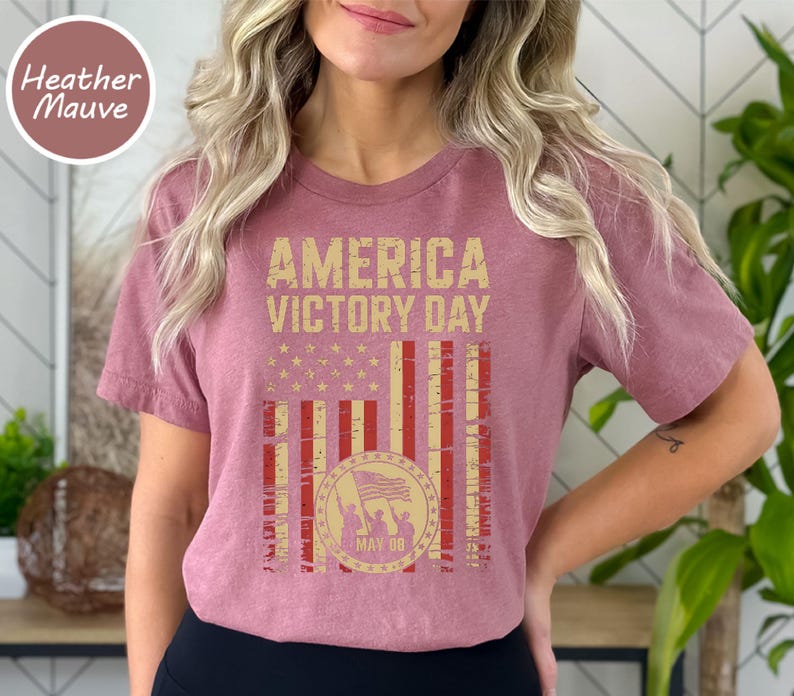 May include: Heather mauve t-shirt with a distressed graphic design. The design features the text "AMERICA VICTORY DAY" above a stylized American flag with a circular emblem. The emblem includes a waving flag and the date "MAY 08".
