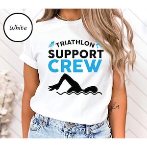 May include: White t-shirt with the words "TRIATHLON SUPPORT CREW" in black and blue. A black silhouette of a swimmer is at the bottom. The word "White" is in a black circle in the upper left corner.
