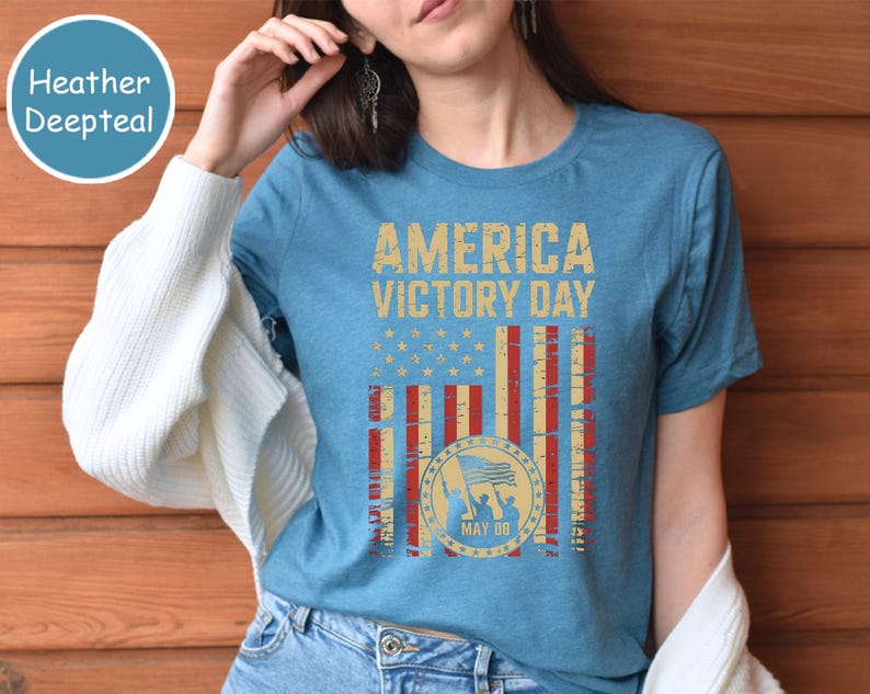 May include: A heather deepteal t-shirt with the words "AMERICA VICTORY DAY" in a distressed gold font. The design includes a flag graphic with red and white stripes, gold stars, and a circular emblem with the date "MAY 08".