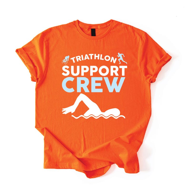 May include: Orange t-shirt with the words "TRIATHLON SUPPORT CREW" in white and light blue. The shirt features a swimmer graphic, a runner graphic, and a bicycle graphic. The shirt is made of a soft material.
