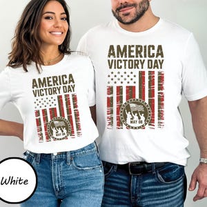 May include: White t-shirts with the text "AMERICA VICTORY DAY" and a distressed American flag design in red, white, and brown. The design includes a circular emblem with figures holding a flag and the date "MAY 08".