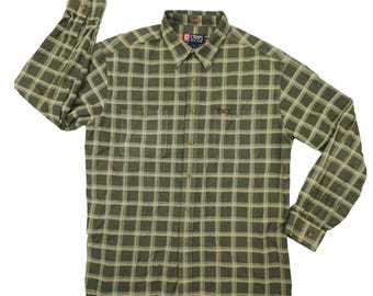 Puede incluir: Camisa de manga larga a cuadros verdes y beige con cierre de botones. La camisa tiene cuello, dos bolsillos en el pecho y puños abotonados. La marca "Chaps" es visible en la etiqueta.
