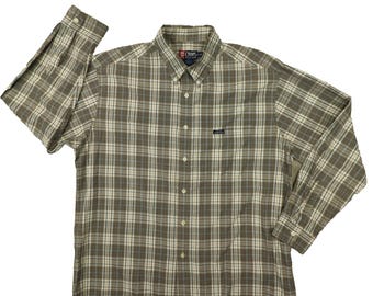 Puede incluir: Camisa abotonada de manga larga con un estampado de cuadros en tonos marrón, beige y blanco. La camisa presenta un cuello abotonado, un bolsillo en el pecho con un pequeño logotipo y puños abotonados. La marca "Chaps" es visible en el cuello.