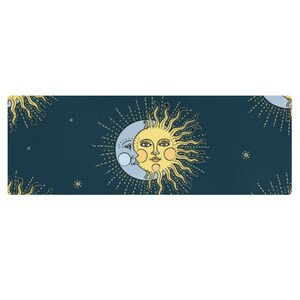 Puede incluir: Una esterilla de yoga rectangular con un diseño celestial. La esterilla tiene un fondo azul oscuro con un patrón repetido de un sol amarillo y una luna azul claro con una cara. Pequeñas estrellas están dispersas por la superficie.