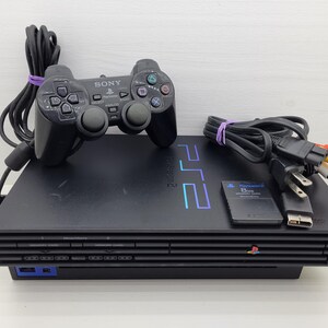 May include: A black Sony PlayStation 2 game console with a matching black wired controller, an 8MB memory card, a power cable, and an AV cable. The console features the blue PS2 logo on the top and the Sony brand name on the front panel.