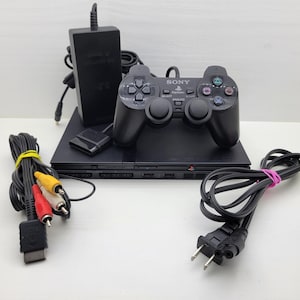 May include: A black Sony PlayStation 2 game console with a matching black DualShock 2 controller, a black power brick, a power cord, and a multi-colored AV cable with yellow, white, and red connectors. The console features the PlayStation logo.