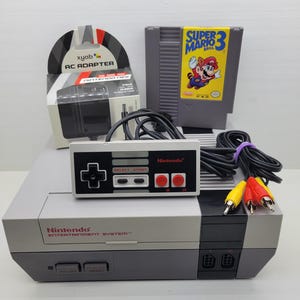 May include: A grey Nintendo Entertainment System console with a controller, a Super Mario Bros. 3 game cartridge, an AC adapter in its box, and AV cables. The console features a front-loading slot, power and reset buttons, and two controller ports.