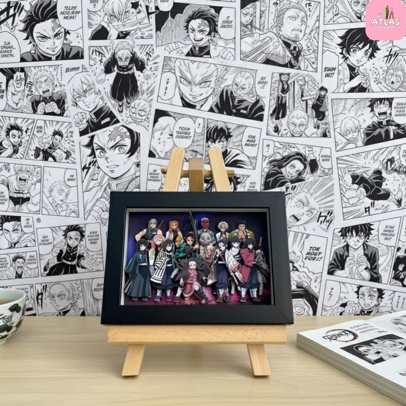 May include: A framed 3D artwork featuring a group of anime characters, displayed on a small wooden easel. The background is a wall covered in black and white manga panels. A teacup and a book are also visible.