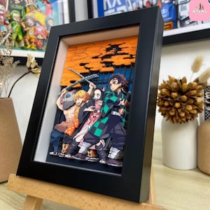 May include: A framed 3D art piece featuring anime characters. The artwork showcases a group of figures in vibrant colors, set against an orange and blue background. The black frame is displayed on a small wooden easel.
