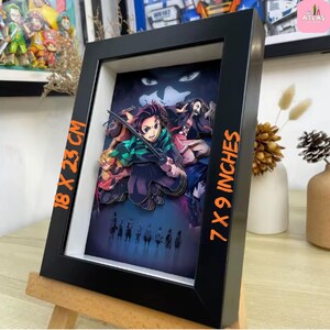 May include: A framed 3D artwork featuring characters from an anime series. The black frame holds a layered paper illustration with vibrant colors. The artwork measures 7 x 9 inches and 18 x 23 cm. The image is displayed on a small wooden easel.