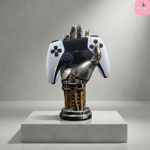 May include: A white and black games controller is held by a metallic robotic hand. The controller has colourful accents and is supported by a detailed, steampunk-style robotic arm and base. The base is a dark, metallic colour.