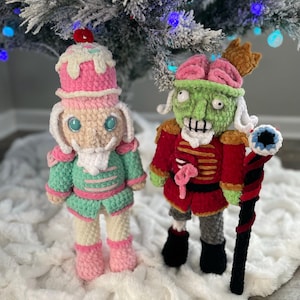 Op de afbeelding: Twee handgemaakte gehaakte figuren: een notenkraker met een roze ijshoornehoed en een zombie met een hersenvormige hoed. De notenkraker draagt een groen en roze uniform. De zombie heeft een rode jas aan en houdt een zwarte staf vast.