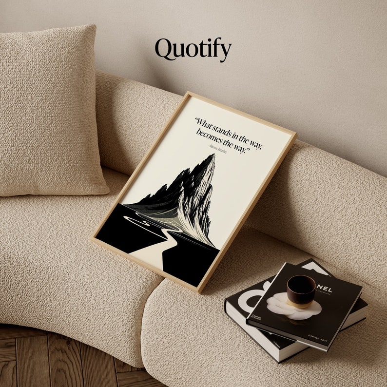 May include: A black and white illustration of a mountain with a winding path leading to the peak. The quote "What stands in the way, becomes the way." by  Marcus Aurelius is printed below the image. The image is framed in a light wood frame and is sitting on a beige couch.