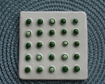 May include: A white ceramic tile with 25 green and white circles arranged in a grid pattern.