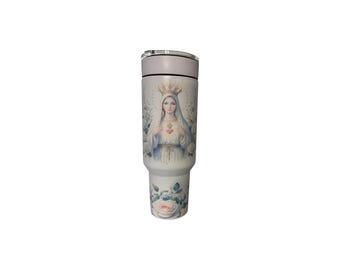 May include: A white tumbler featuring a religious illustration of a woman with a crown and a heart. The design includes floral elements and is set against a white background. The tumbler has a silver lid.