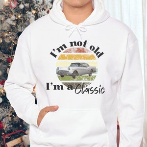 May include: White hooded sweatshirt with a vintage-style graphic of a car and the text "I'm not old I'm a classic".