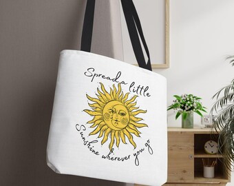 Peut inclure: Sac fourre-tout blanc avec des poignées noires représentant un soleil jaune avec un visage et le texte "Spread a little sunshine wherever you go."