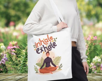 May include: White tote bag with the text "inhale exhale" in colorful letters. A cartoon illustration of a person meditating with flowers and leaves around them.